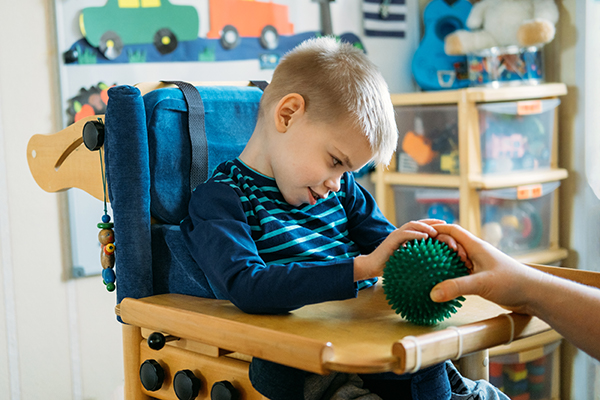 Sensory Activities for kids with disabilities. Preschool Activities for Children with Special Needs. Boy with with Cerebral Palsy in special chair play with mom at home