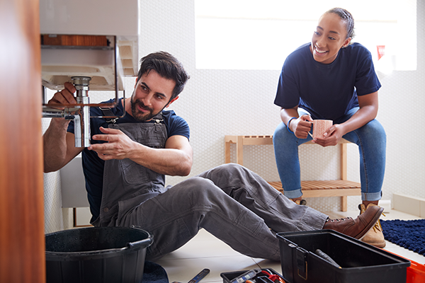 Male Plumber Teaching Female Apprentice To Fix Leaking Sink In Home Bathroom