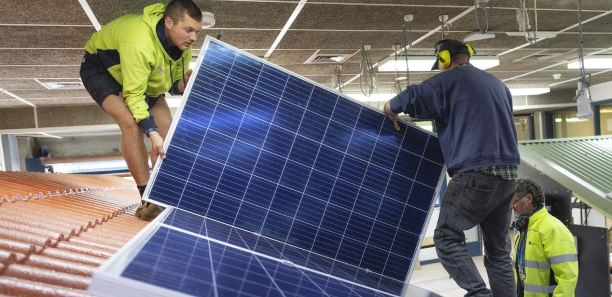 Students fitting a solar panel on a roof top