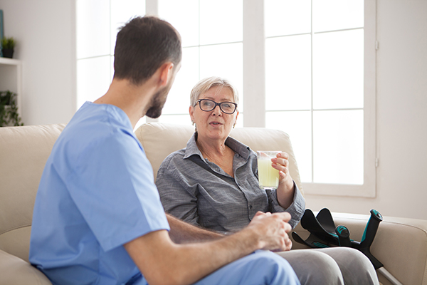 Doctor sitting on couch in nursing home talking with senior woman with crutches while she&#39;s taking her pills.